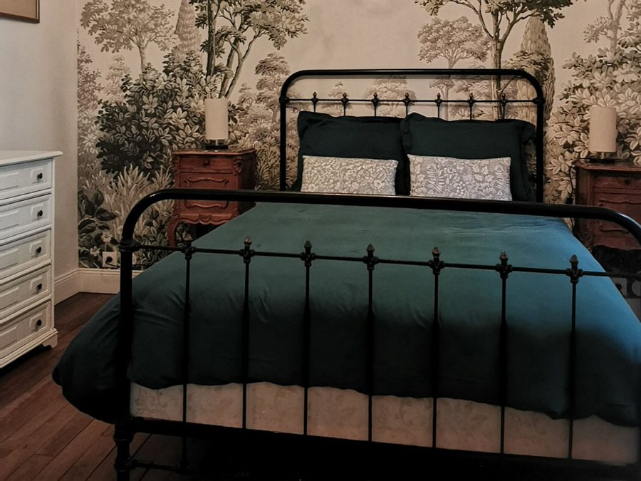 La Chambre du Loiret : lit en fer forgé, papier peint à motif d'arbres et lustre