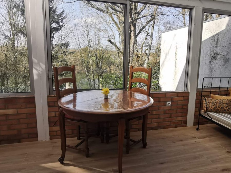 La véranda de la maison : table ronde et vue sur le Loiret à travers les grandes baies vitrées